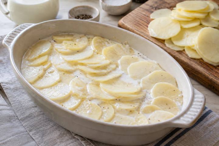 器に薄切りのじゃがいもを重ね、牛乳と生クリームを注いだ焼く前のグラタン